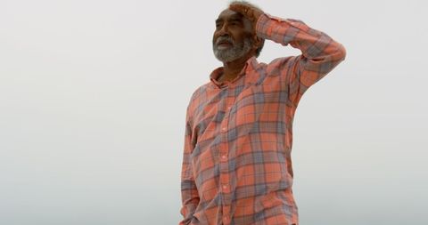 Senior Man Walking on Beach Shielding Sunlight with Hand