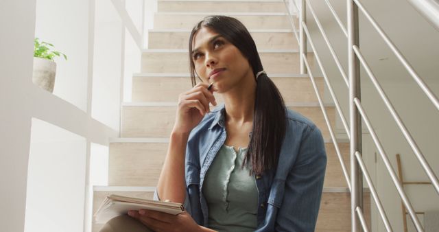 Young woman ponderously sitting on stairs, dressed casually. Ideal for concepts related to education, studying, planning, contemplation, and thoughtful moments. Suitable for educational materials, blogs discussing productivity or mindfulness, and lifestyle articles.
