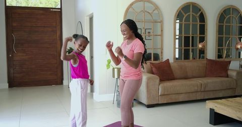 African american mother and daughter exercising on purple yoga mat in living room, smiling