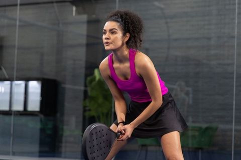 Focused african american woman playing indoor pickleball in magenta tank and black skirt