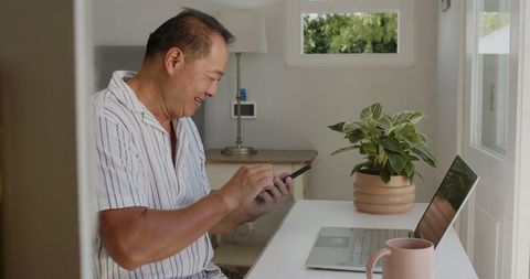 Man smiling while using smartphone and laptop at home