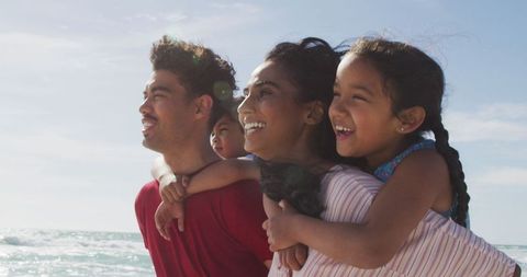 Happy Family Enjoying Day at Beach with Children on Piggyback