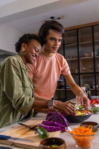 Diverse couple preparing fresh salad together in cozy modern kitchen, healthy meal prep