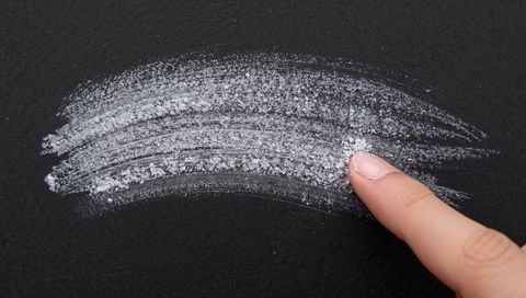 Index finger dragging chalk dust creating white textured streak across black matte surface