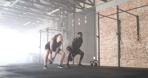 Diverse Workout Partners Lifting Kettlebells at CrossFit Gym