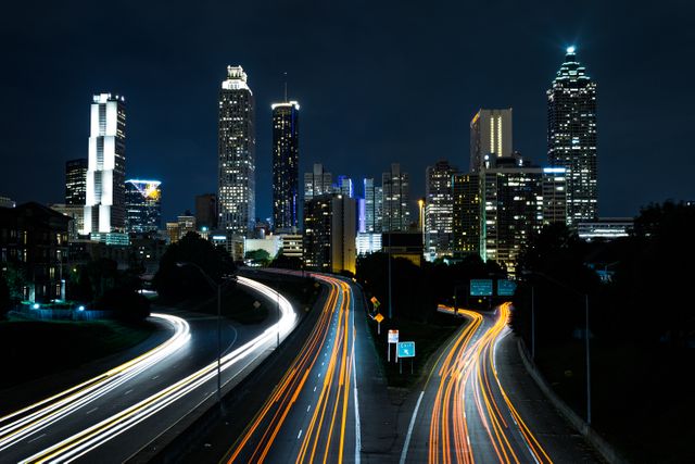 Downtown city skyline featuring tall buildings and light trails from traffic on highways at night. Useful for urban themes, travel blogs, articles on nightlife, business, and architecture presentations.