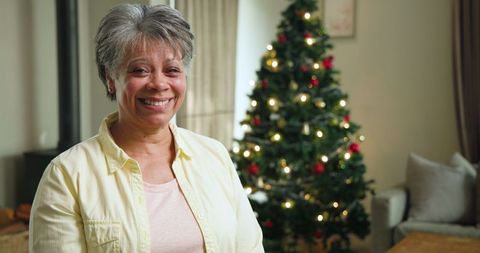 Senior woman smiling by decorated christmas tree in cozy living room