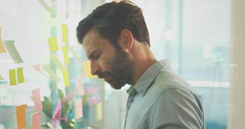 Focused man planning with colorful sticky notes on glass wall in modern coworkorking office