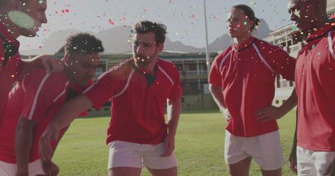 Huddling and celebrating male athletes wearing red jerseys and white shorts with confetti