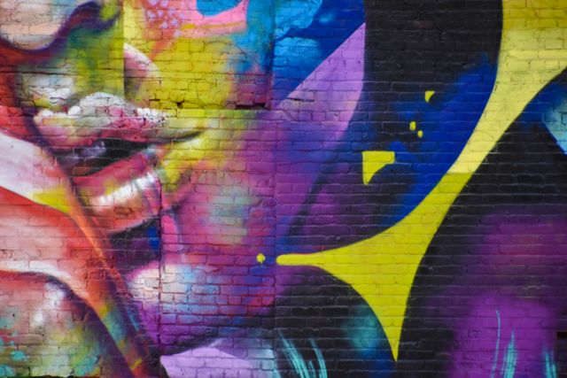 The photo features a colorful and vibrant piece of urban street art on a brick wall. The composition includes abstract shapes with bright colors like yellow, pink, purple, and blue. This type of image is useful for illustrating creativity, urban culture, and contemporary art in various digital and print media such as blog articles, magazines, art websites, and promotional materials for cultural events.