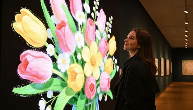 Museum visitor observing giant led floral artwork with tulips and daisies in dark gallery