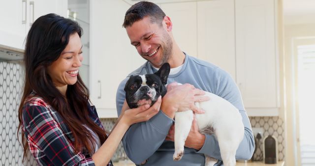 A joyful couple enjoys bonding with their French Bulldog in a modern kitchen. Great for themes around domestic life, pet ownership, happy relationships, modern homes, and emotional connections.