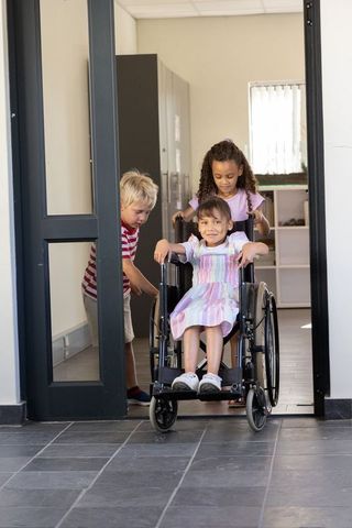 Children pushing wheelchair through classroom doorway promoting inclusion and accessibility