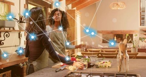 Friends preparing fresh salad and pouring drinks in sunlit rustic home kitchen
