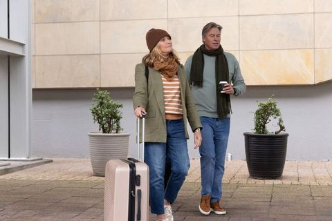Mature couple walking pulling suitcase holding coffee in urban weekend getaway