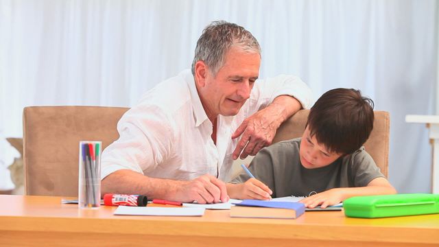 Grandfather sit at table with grandson, actively engaged in education. Perfect for illustrating family education dynamics, multigenerational bonding, or support in home schooling contexts.