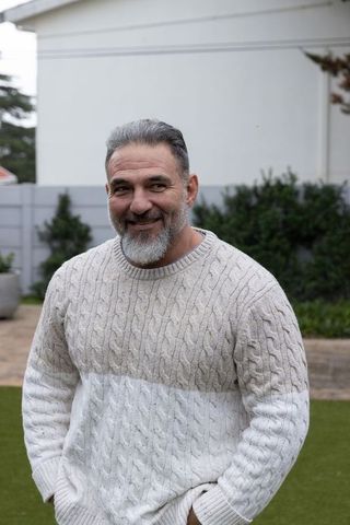 Smiling senior man wearing two-tone cable-knit sweater standing in backyard garden