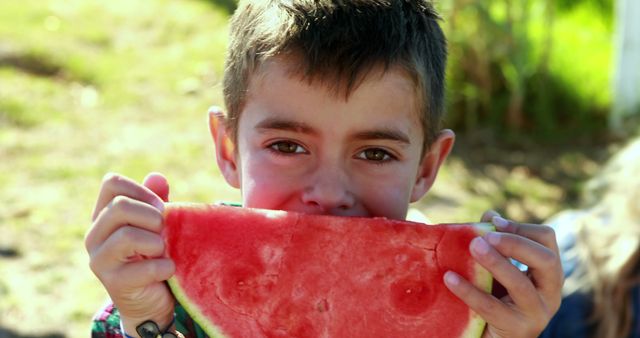A young Caucasian boy is enjoying a large slice of watermelon outdoors, with copy space. His joyful expression and the summery snack evoke a sense of carefree childhood and seasonal fun.