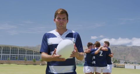 Confident rugby player holding ball with team huddling