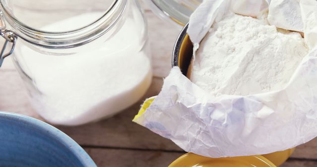 This image shows flour wrapped in parchment paper next to a jar of sugar, likely on a wooden countertop. It is ideal for illustrating baking recipes, kitchen scenes, or articles related to cooking and food preparation.