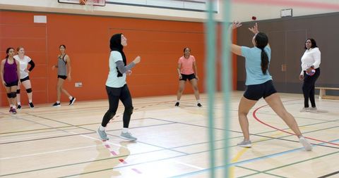 Diverse women training volleyball indoors during competitive team drill with coach guidance