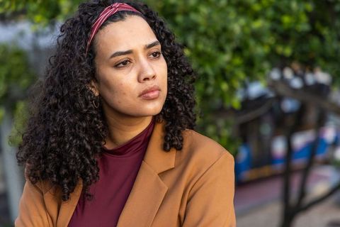 Young woman wearing tan blazer and red headband looking thoughtful in urban transit