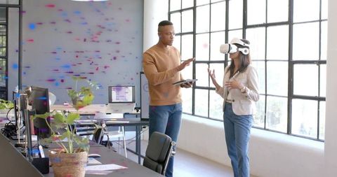 Mentor guiding colleague testing virtual reality headset in bright modern office workspace