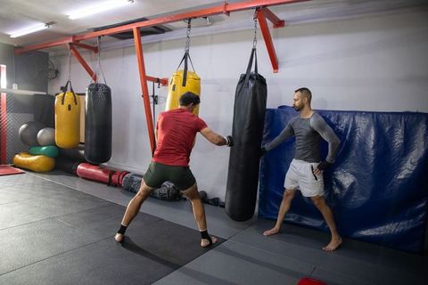 Male training partners practicing heavy bag strikes in martial arts gym session