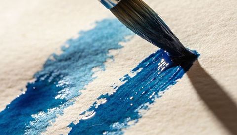 Macro watercolor brush applying vibrant blue wash on cold-press paper texture