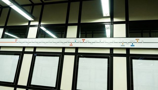 Transit map strip running across platform with black grid, backlit panels and reflections