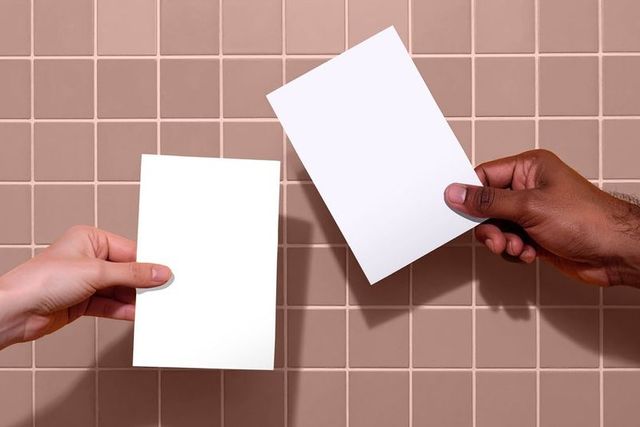 Two hands holding blank papers against peach tiled wall