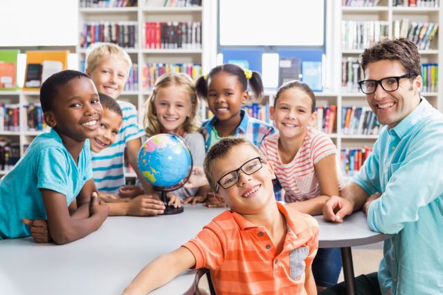 Diverse group of children and their teacher smiling in a library, gathered around a globe. Ideal for educational materials, school brochures, multicultural learning resources, and classroom posters.