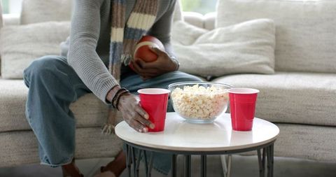 Mid-adult African-American man reaching for red cup on coffee table with popcorn and football
