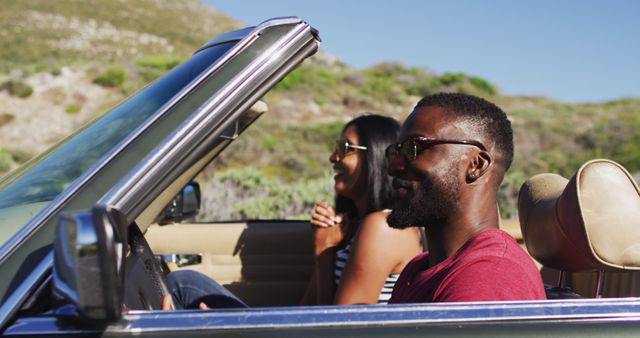 African american couple talking to each other while sitting in convertible car on road. road trip travel and adventure concept