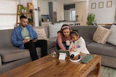 Multicultural family helping daughter with homework on tablet in cozy modern living room