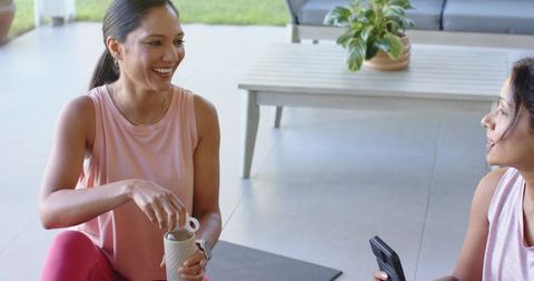 Smiling women chatting after outdoor workout on patio stirring tumbler during cool down