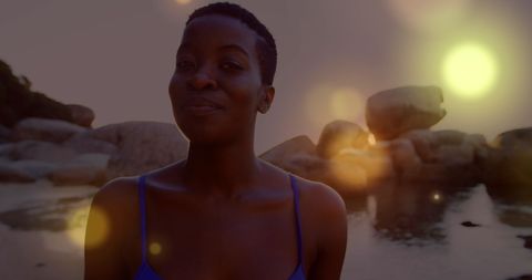 African american woman strolling by rocky seashore at sunset
