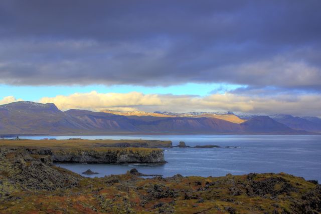 This serene coastal scene showcases the Icelandic landscape with its pristine waters, mountainous terrain, and dramatic, cloud-filled sky. Perfect for travel posters, nature brochures, and websites focusing on outdoor adventures or eco-tourism. The rugged terrain and vibrant landscape make it ideal for inspiring scenic prints and digital wallpapers.