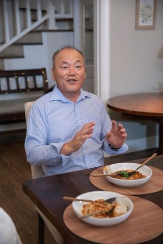 Mature asian man gesturing and speaking at dining table with noodle bowls during dinner