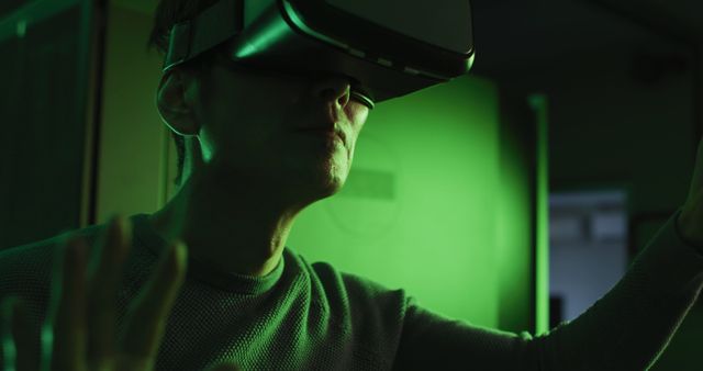 Person exploring a virtual reality experience wearing VR headset, surrounded by green light. Ideal for use in technology blogs, articles about virtual and augmented reality, digital innovation showcases, gaming websites, and promotional materials related to futuristic gear.