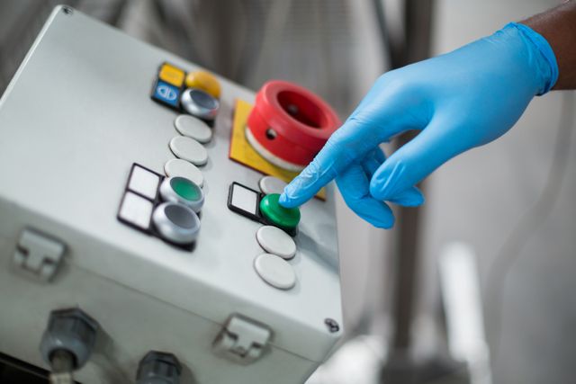 Hand of factory engineer pressing button on control panel in industrial setting. Useful for illustrating concepts of automation, manufacturing processes, industrial safety, and engineering operations.