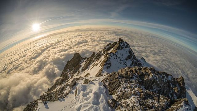 Overlooking jagged alpine ridge above sea of clouds, snow cornices and footprints at sunrise