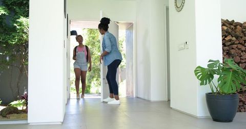 African mother greeting daughter returning from school at bright modern foyer