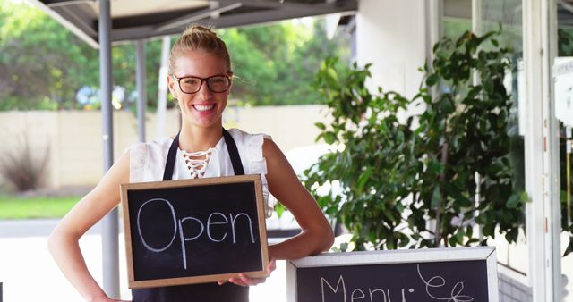 Portrait of waitress holding a chalkboard with open sign outside the cafe 4k
