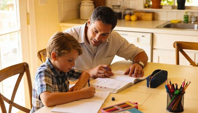 Father helping son with homework at kitchen table, tutoring and mentoring moment