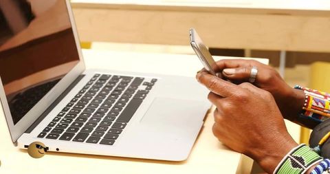 Hands Holding Smartphone Over Laptop Showing Beaded Bracelets Workspace Productivity and Mobile Focu