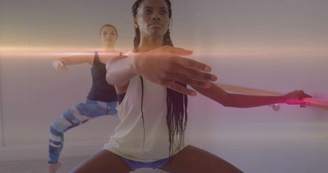 Squatting women practicing barre balance and arm extension in minimalist dance studio