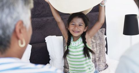 Joyful girl holding hat playing on bed at home with grandparents