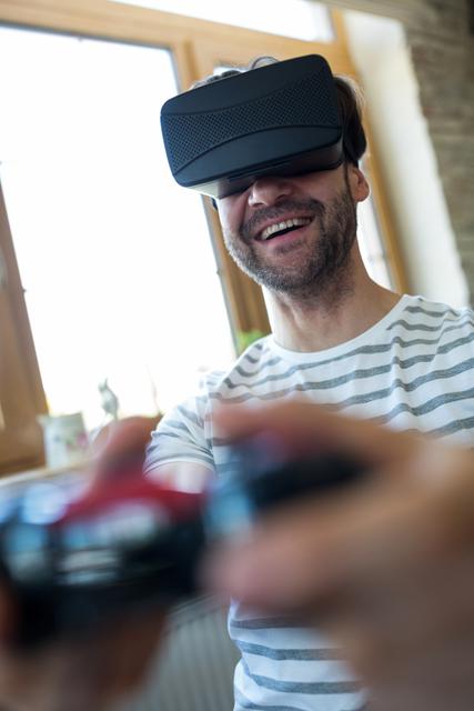 Man immersed in virtual reality gaming experience while smiling at a coffee shop. Suitable for technology, leisure, and lifestyle marketing materials. Perfect for promoting VR headsets, gaming gear, and modern entertainment activities.