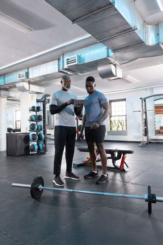 African american trainer coaching client with tablet in modern gym strength session